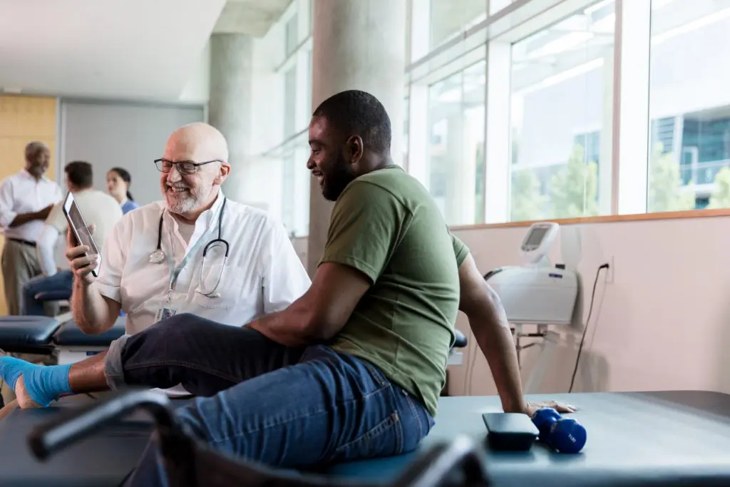 Male patient and mature doctor smile at information on tablet