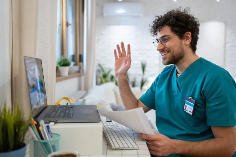 Male nurse in scrubs, waving back to a patient during an video call