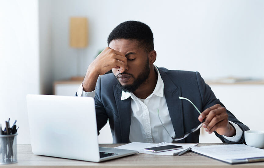 Person holding the bridge of their nose looking at their laptop frustrated