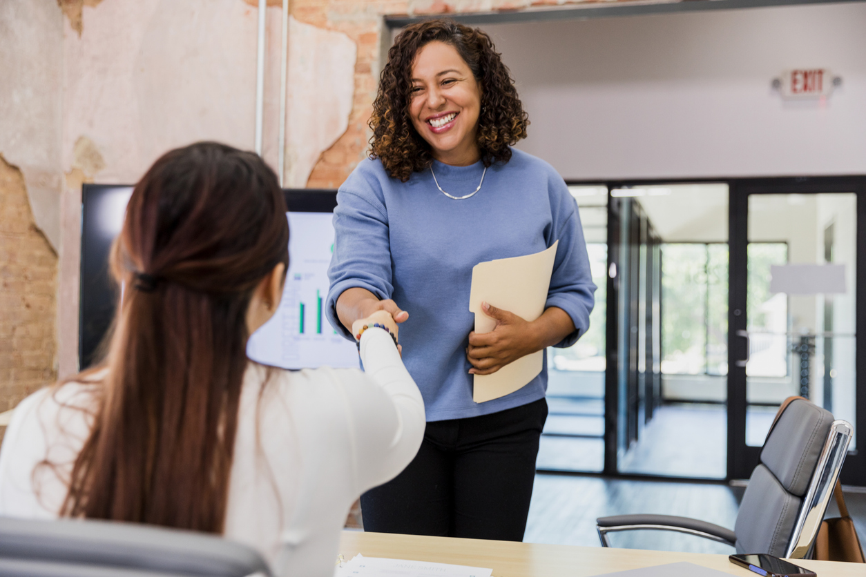 Businesswoman shaking hands, smiling, office meeting healthcare staff collecting SDOH screening info at the front desk