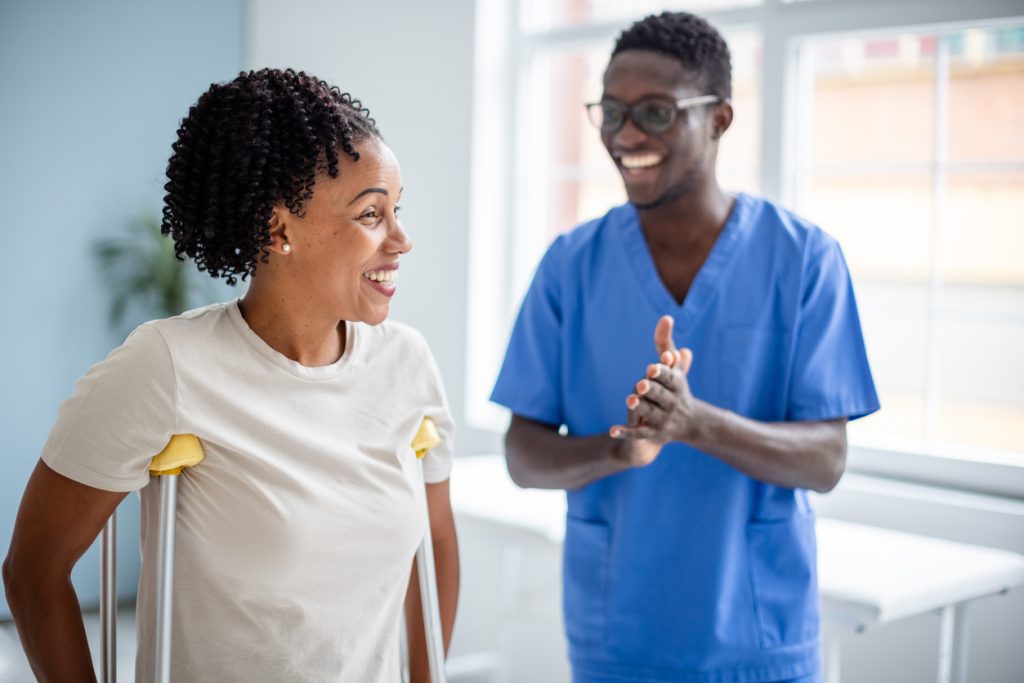Smiling woman on crutches with supportive therapist